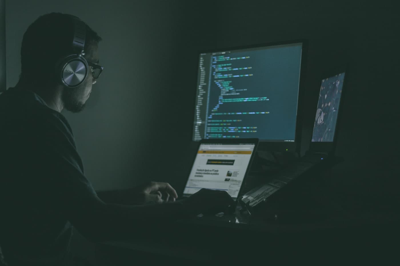 Engineer focused at laptop with headphones in dark office